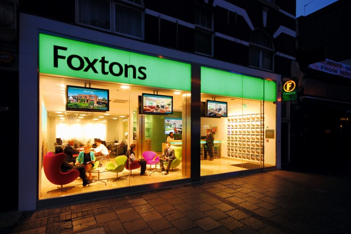 A Foxtons office lit up at night with business people inside.